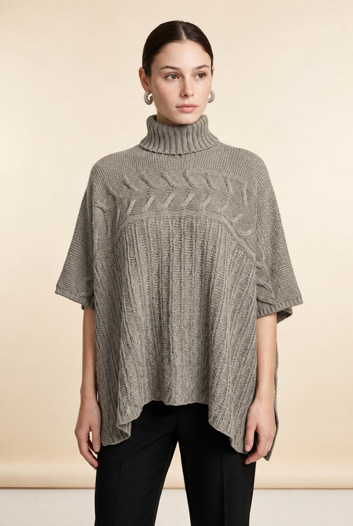 A woman wearing the Aosta cable-knit turtleneck sweater in taupe, highlighting its ribbed lower body and wide sleeves.
