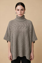 A woman wearing the Aosta cable-knit turtleneck sweater in taupe, highlighting its ribbed lower body and wide sleeves.