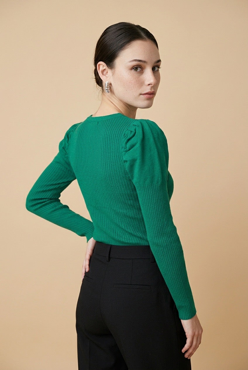 A woman wearing the Arezzo green knit top with long sleeves, puff shoulders, and a V-neckline, styled with black tailored trousers.