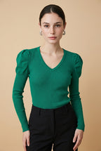 A woman wearing the Arezzo green knit top with long sleeves, puff shoulders, and a V-neckline, styled with black tailored trousers.
