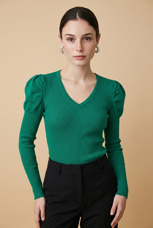 A woman wearing the Arezzo green knit top with long sleeves, puff shoulders, and a V-neckline, styled with black tailored trousers.