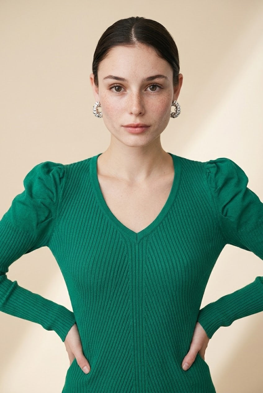 A woman wearing the Arezzo green knit top with long sleeves, puff shoulders, and a V-neckline, styled with black tailored trousers.