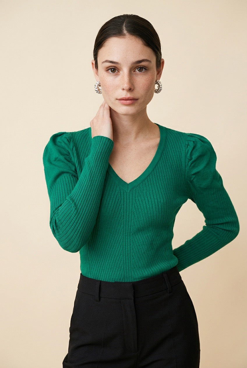 A woman wearing the Arezzo green knit top with long sleeves, puff shoulders, and a V-neckline, styled with black tailored trousers.