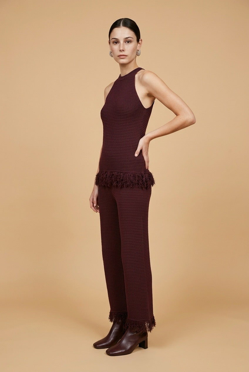 A woman wearing the Set Bérgamo knit two-piece set in deep burgundy, featuring a sleeveless halter top and straight-leg trousers with fringe hem details.