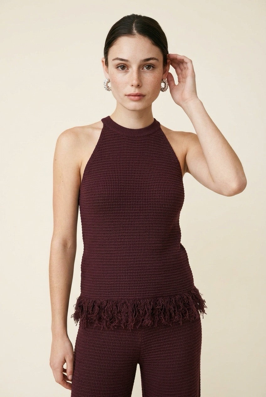 A woman wearing the Set Bérgamo knit two-piece set in deep burgundy, featuring a sleeveless halter top and straight-leg trousers with fringe hem details.
