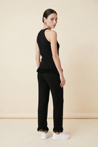 A woman wearing the Set Bérgamo knit two-piece set in black, featuring a sleeveless halter top and straight-leg trousers with fringe hem details.