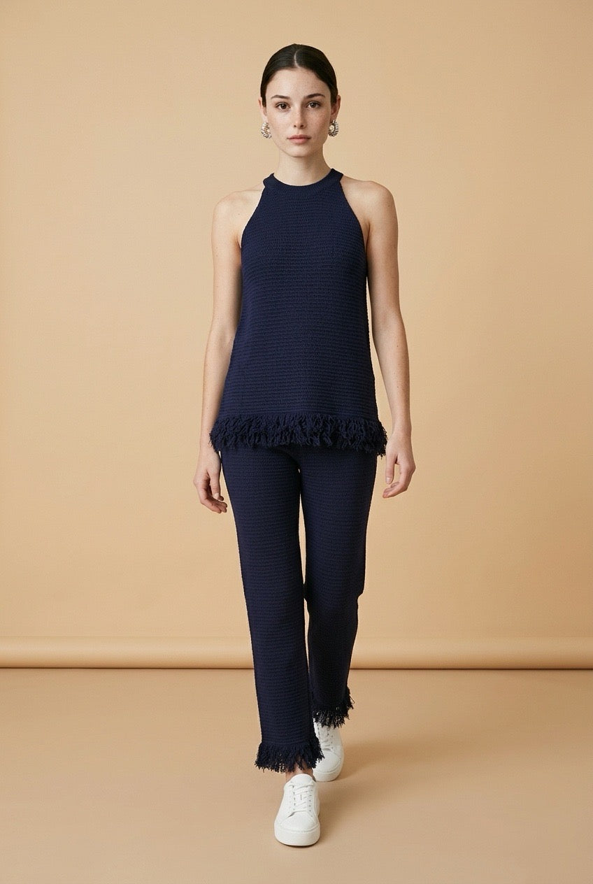 A woman wearing the Set Bérgamo knit two-piece set in navy blue, featuring a sleeveless halter top and straight-leg trousers with fringe hem details.