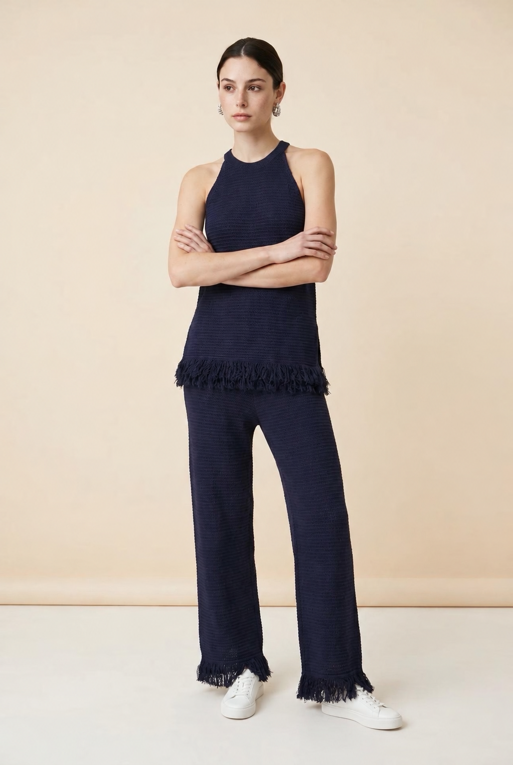 A woman wearing the Set Bérgamo knit two-piece set in navy blue, featuring a sleeveless halter top and straight-leg trousers with fringe hem details.
