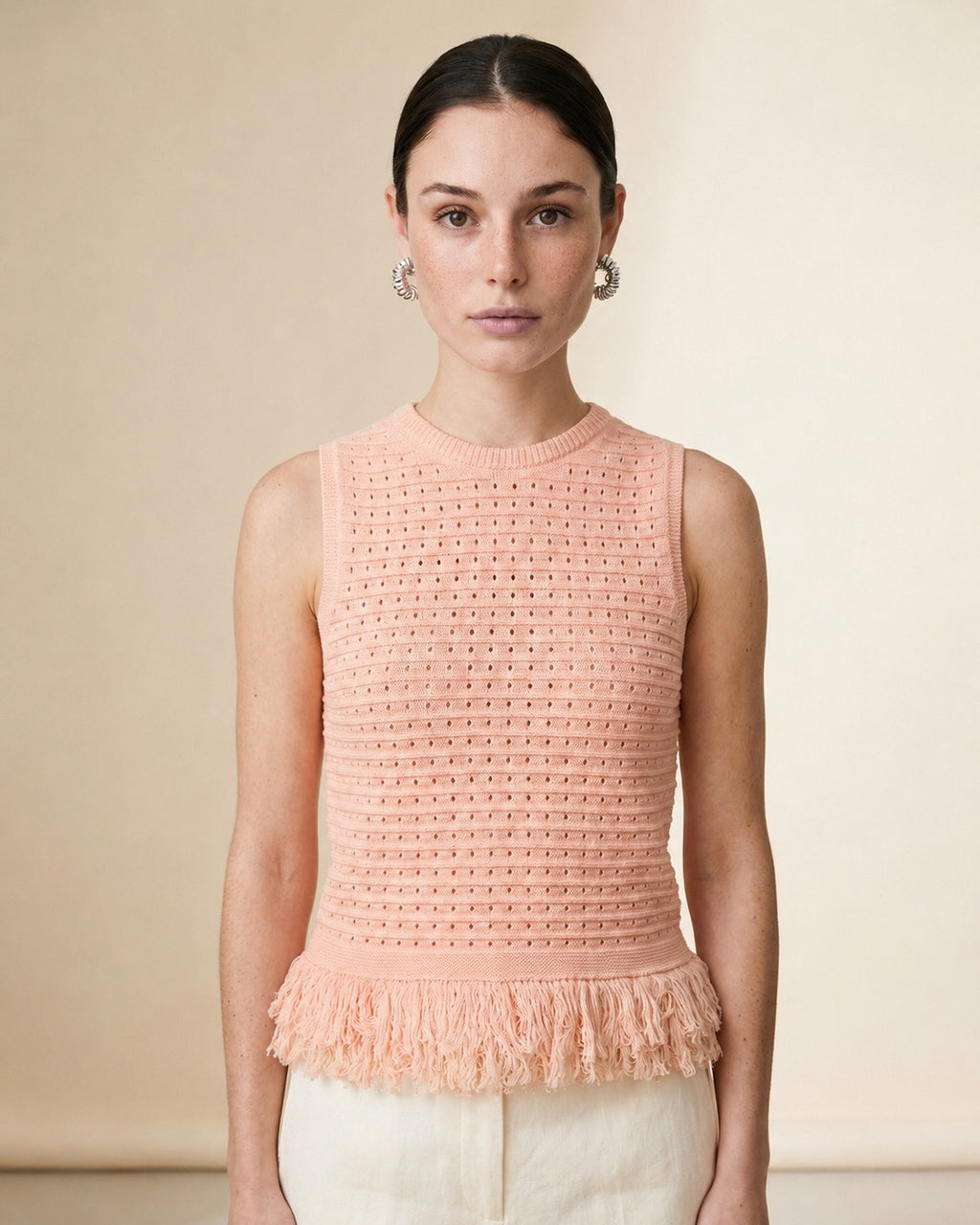 Woman wearing the Amelia sleeveless open-knit tank top in soft pink with a fringed peplum hem