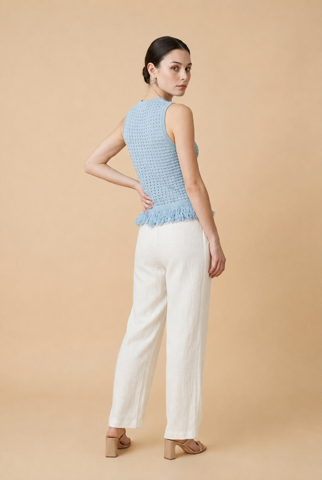Woman wearing the Amelia sleeveless open-knit tank top in light blue with a fringed peplum hem