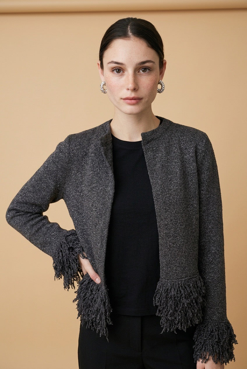 A woman wearing the open-front Cervinia knit cardigan in grey, featuring textured fringe trim along the hemline and sleeve cuffs.