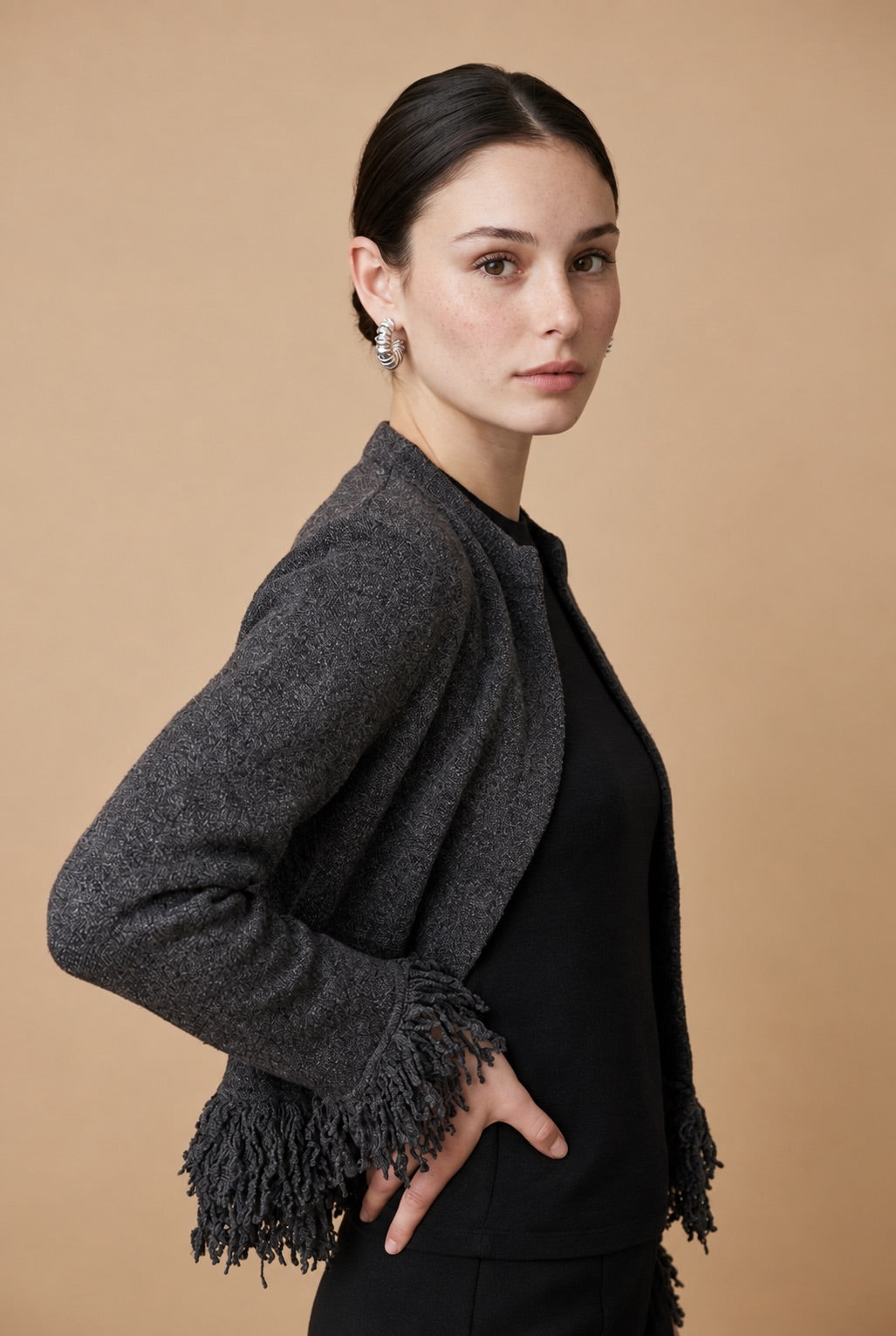 A woman wearing the open-front Cervinia knit cardigan in grey, featuring textured fringe trim along the hemline and sleeve cuffs.