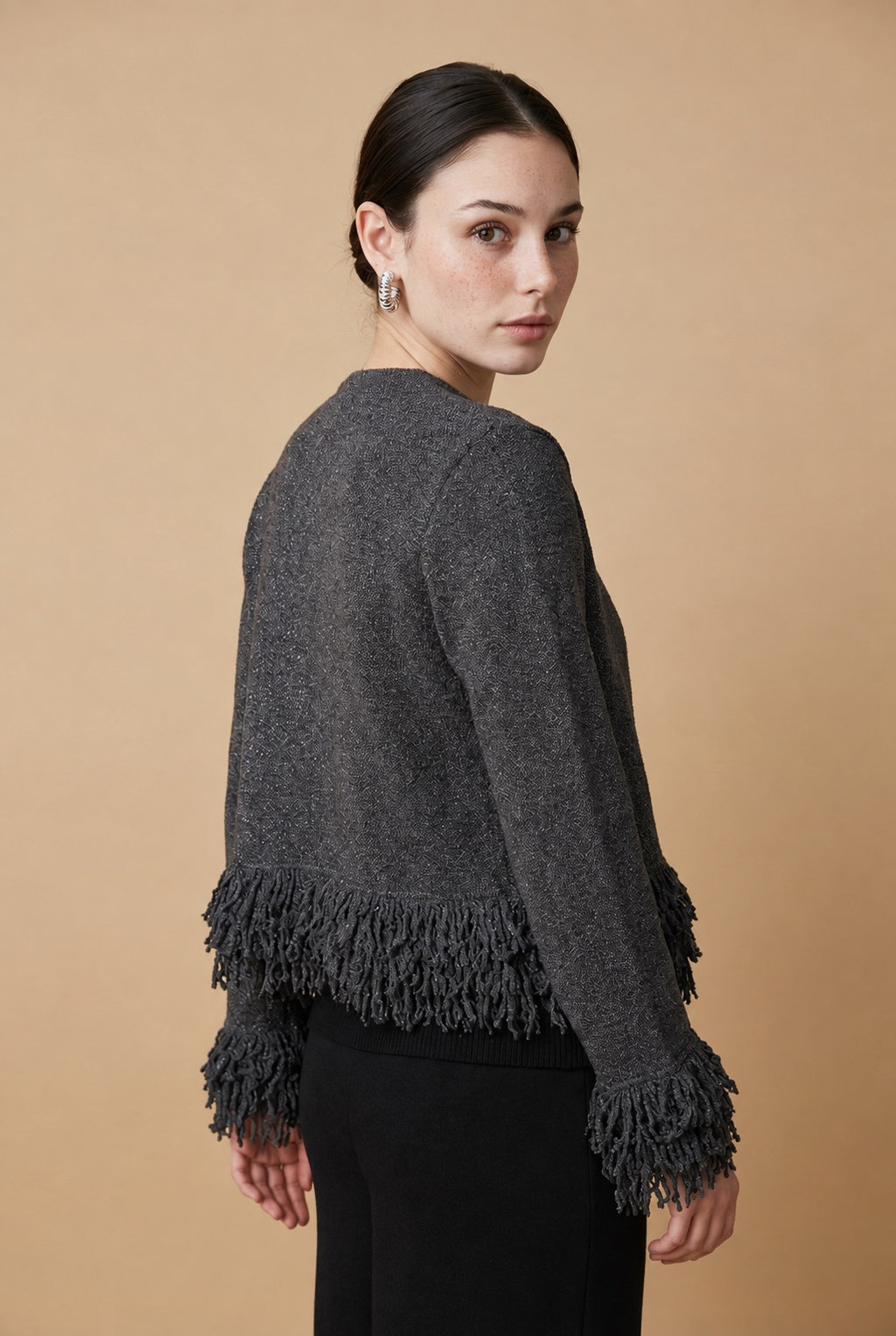 A woman wearing the open-front Cervinia knit cardigan in grey, featuring textured fringe trim along the hemline and sleeve cuffs.