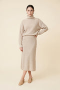 A woman wearing the Ginevra two-piece ribbed knit set in beige, featuring a turtleneck sweater and matching midi skirt.