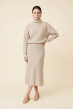 A woman wearing the Ginevra two-piece ribbed knit set in beige, featuring a turtleneck sweater and matching midi skirt.
