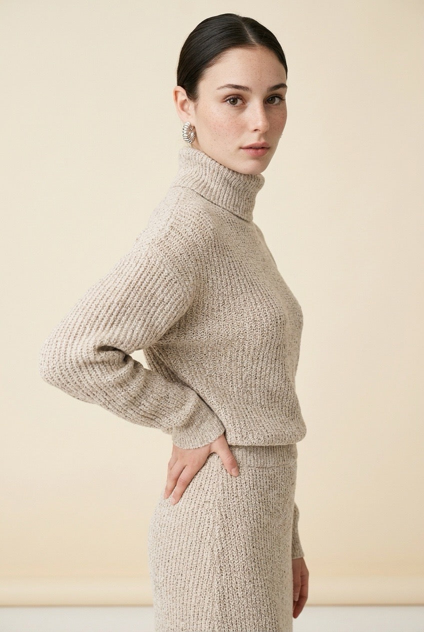 A woman wearing the Ginevra two-piece ribbed knit set in beige, featuring a turtleneck sweater and matching midi skirt.