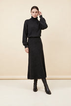 A woman wearing the Ginevra two-piece ribbed knit set in black, featuring a turtleneck sweater and matching midi skirt.