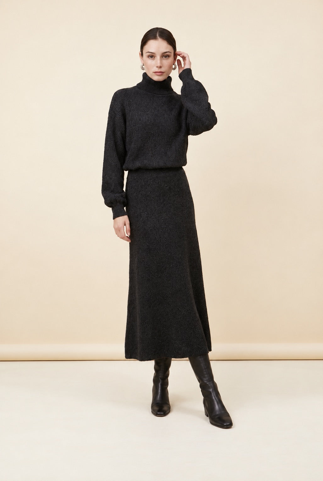 A woman wearing the Ginevra two-piece ribbed knit set in black, featuring a turtleneck sweater and matching midi skirt.