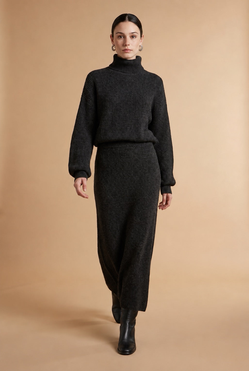 A woman wearing the Ginevra two-piece ribbed knit set in black, featuring a turtleneck sweater and matching midi skirt.