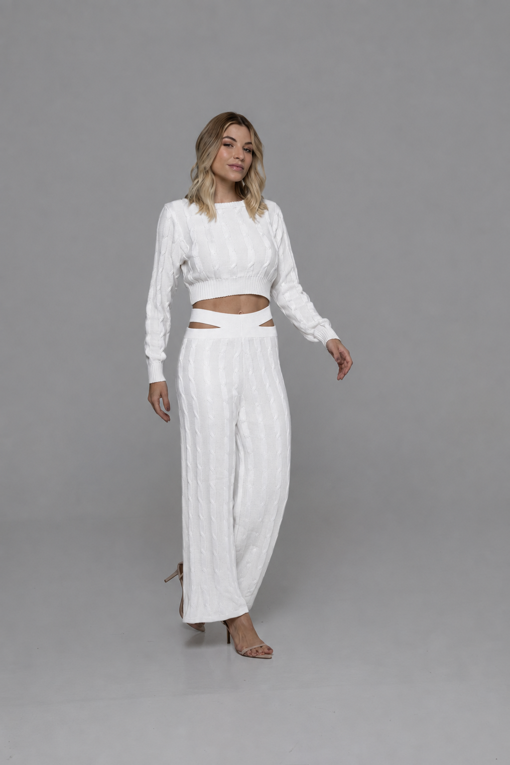 Casa Maly Bacana Set - White cable-knit crop top and matching trousers with distinctive waist cutouts, worn by a model on a Mediterranean balcony overlooking Portofino at sunset.
