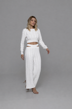 Casa Maly Bacana Set - White cable-knit crop top and matching trousers with distinctive waist cutouts, worn by a model on a Mediterranean balcony overlooking Portofino at sunset.
