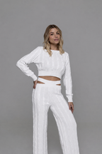 Casa Maly Bacana Set - White cable-knit crop top and matching trousers with distinctive waist cutouts, worn by a model on a Mediterranean balcony overlooking Portofino at sunset.