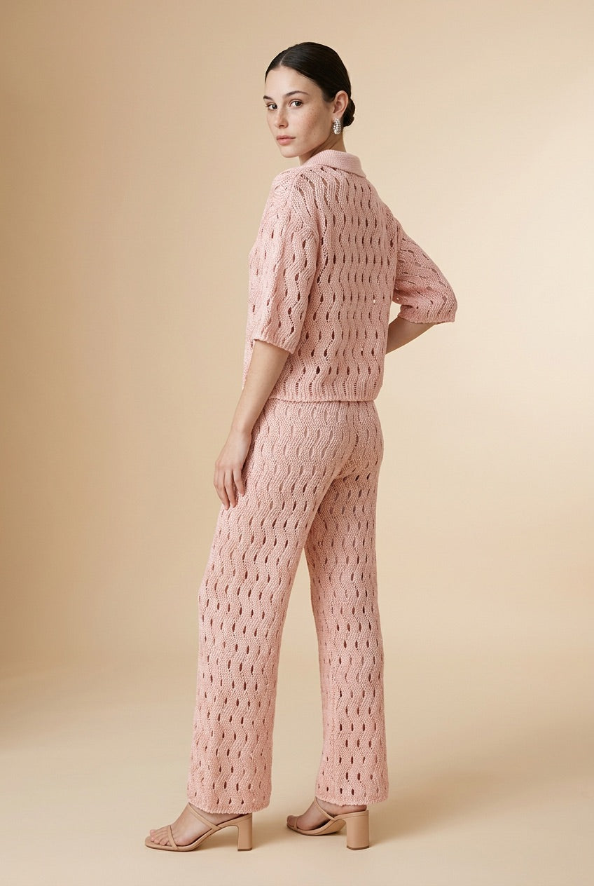 A woman wearing the Set Positano open-knit two-piece set in light pink, featuring a collared polo top and matching wide-leg trousers.