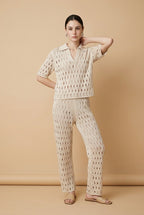 A woman wearing the Set Positano open-knit two-piece set in beige, featuring a collared polo top and matching wide-leg trousers.