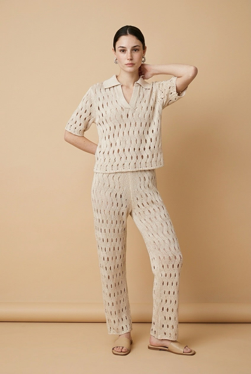 A woman wearing the Set Positano open-knit two-piece set in beige, featuring a collared polo top and matching wide-leg trousers.