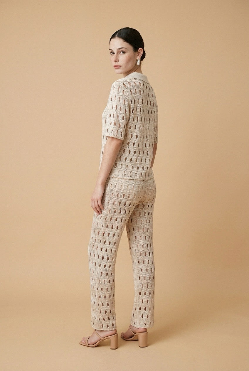 A woman wearing the Set Positano open-knit two-piece set in beige, featuring a collared polo top and matching wide-leg trousers.