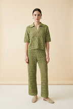 A woman wearing the Set Positano open-knit two-piece set in olive green, featuring a collared polo top and matching wide-leg trousers.