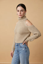 A woman wearing the Livigno cold-shoulder turtleneck sweater in beige, showing the textured chevron knit and high-neck silhouette.