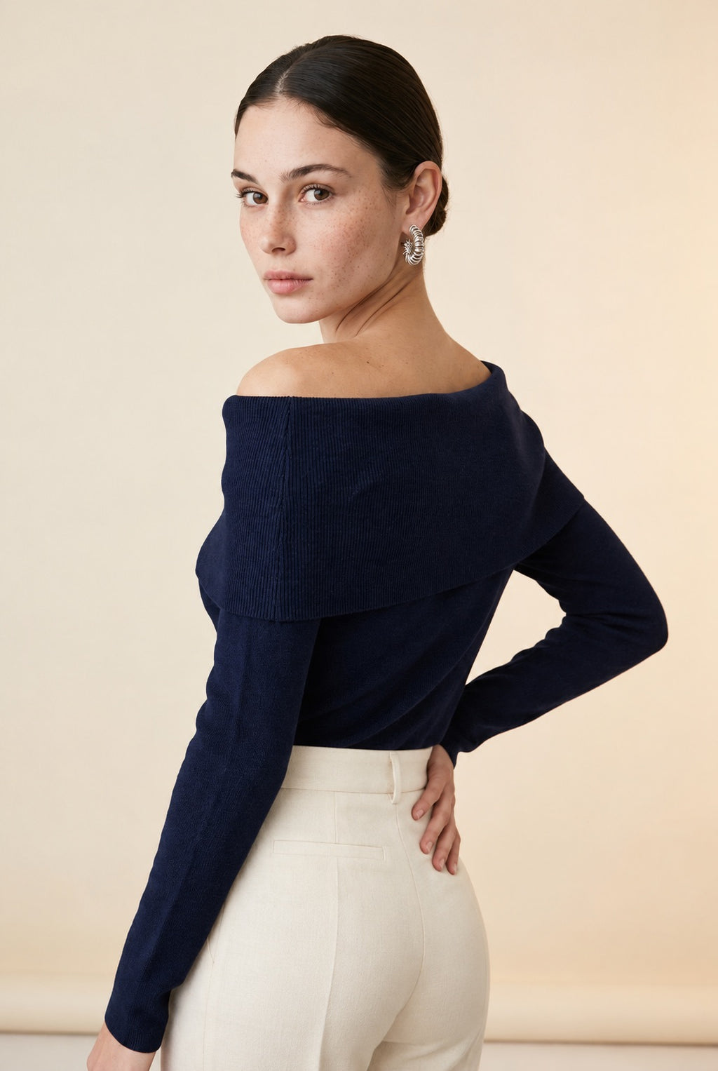 A woman wearing the Top Lecce off-the-shoulder knit top in navy blue, showing its sleek fitted silhouette.