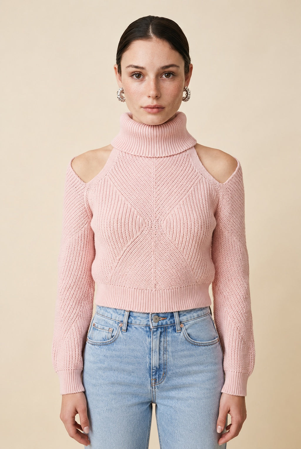 A woman wearing the Livigno cold-shoulder turtleneck sweater in baby pink, highlighting its intricate knit detail and open-shoulder cuts.