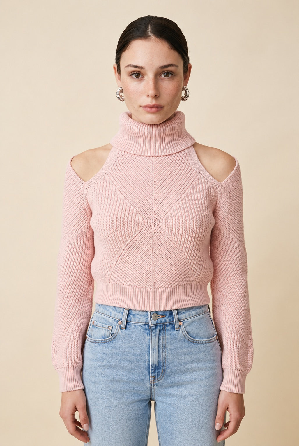 A woman wearing the Livigno cold-shoulder turtleneck sweater in baby pink, highlighting its intricate knit detail and open-shoulder cuts.