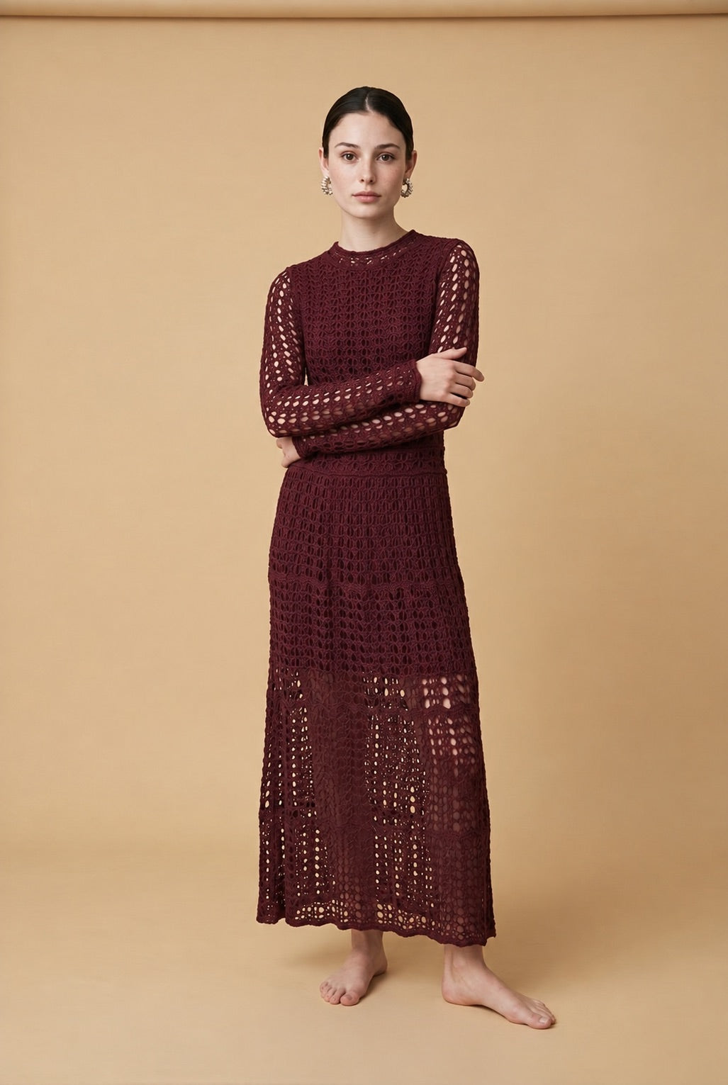 A woman wearing the chic long-sleeved Jackie midi dress in burgundy, accentuating its intricate geometric lace knit patterns.