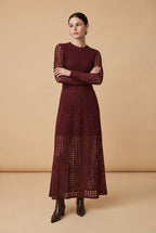 A woman wearing the chic long-sleeved Jackie midi dress in burgundy, accentuating its intricate geometric lace knit patterns.