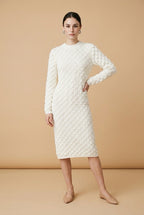 A woman wearing the Lucce long-sleeve knit midi dress in off-white, featuring a prominent 3D scallop cable texture and a classic crew neck.
