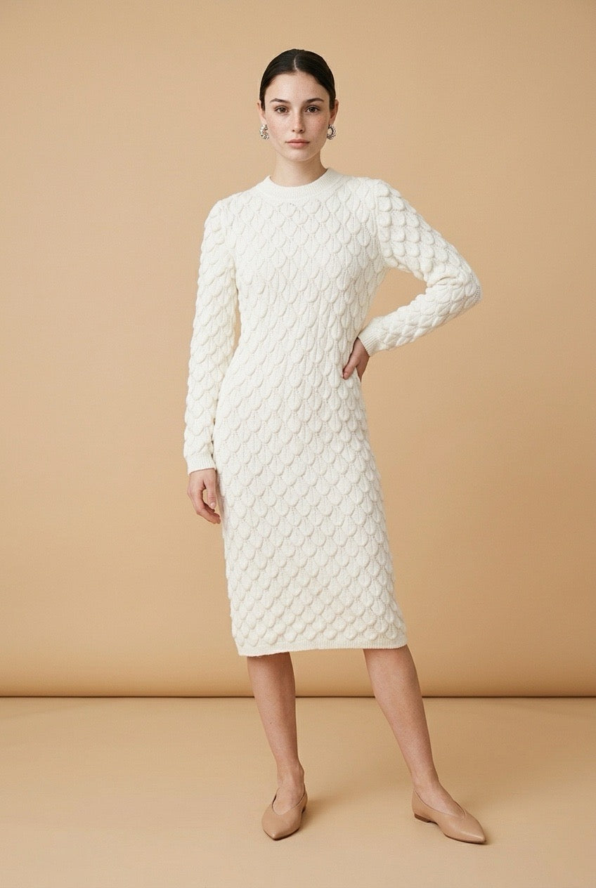 A woman wearing the Lucce long-sleeve knit midi dress in off-white, featuring a prominent 3D scallop cable texture and a classic crew neck.