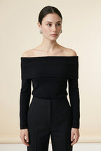 A woman wearing the Top Lecce off-the-shoulder knit top in black, featuring a foldover neckline and slim long sleeves.