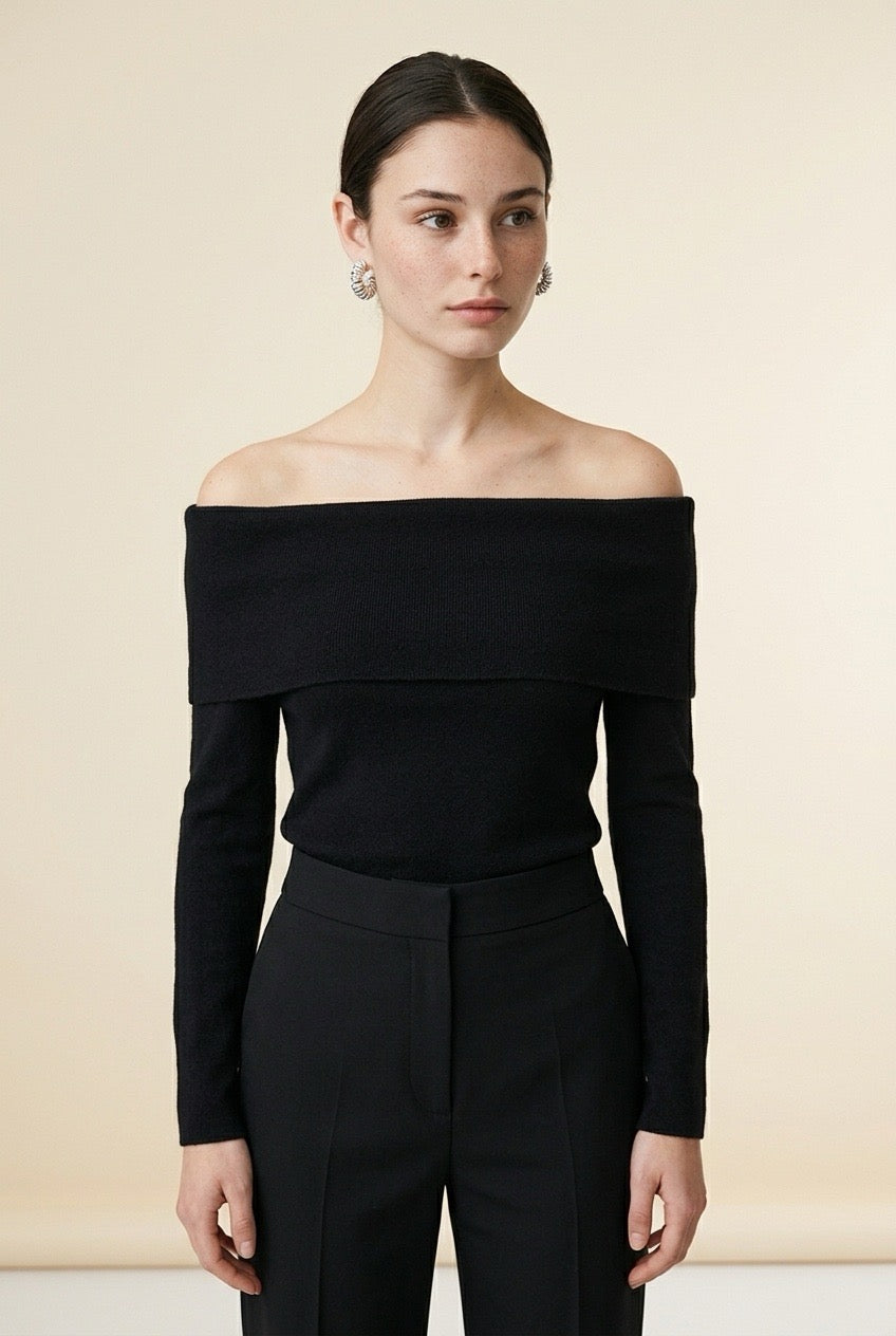 A woman wearing the Top Lecce off-the-shoulder knit top in black, featuring a foldover neckline and slim long sleeves.
