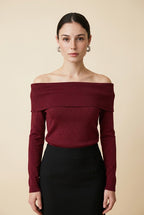 A woman wearing the Top Lecce off-the-shoulder knit top in burgundy shimmer, paired with a black tailored skirt.