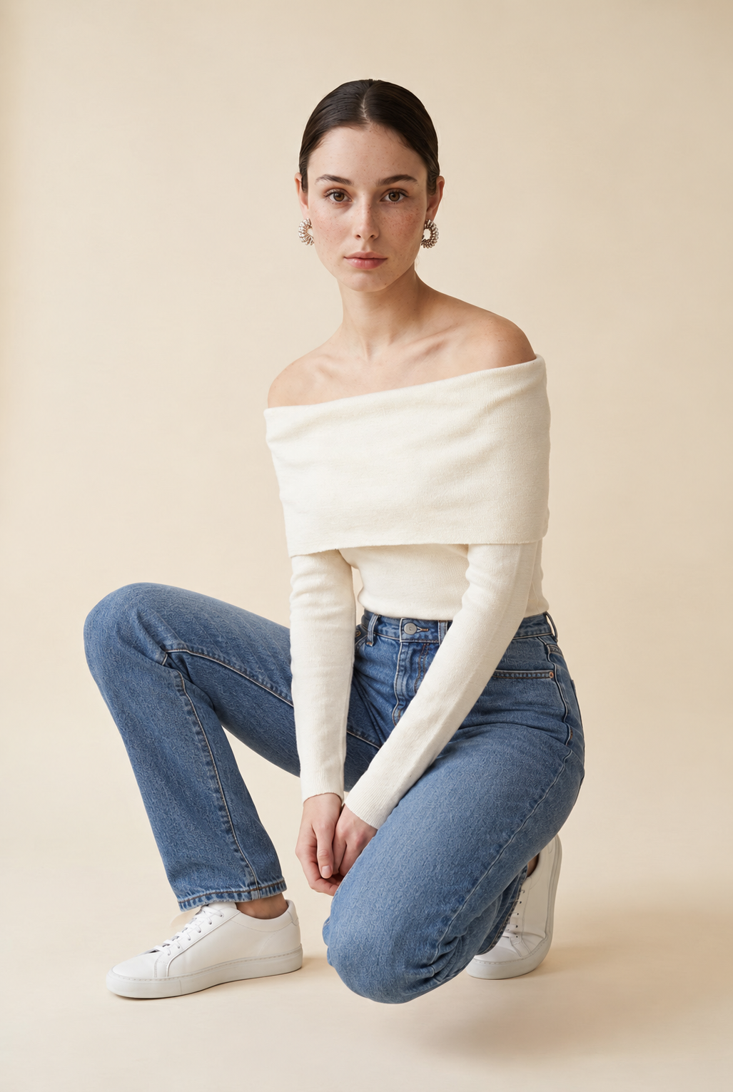 A woman wearing the Top Lecce off-the-shoulder knit top in off white, highlighting the subtle textured knit.