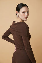 A woman wearing the Top Lecce off-the-shoulder knit top in deep brown, styled for a chic modern look.