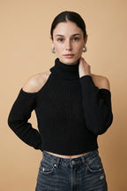 A woman wearing the Livigno cold-shoulder turtleneck sweater in black, showcasing its chic cut-outs and wide ribbed hem.