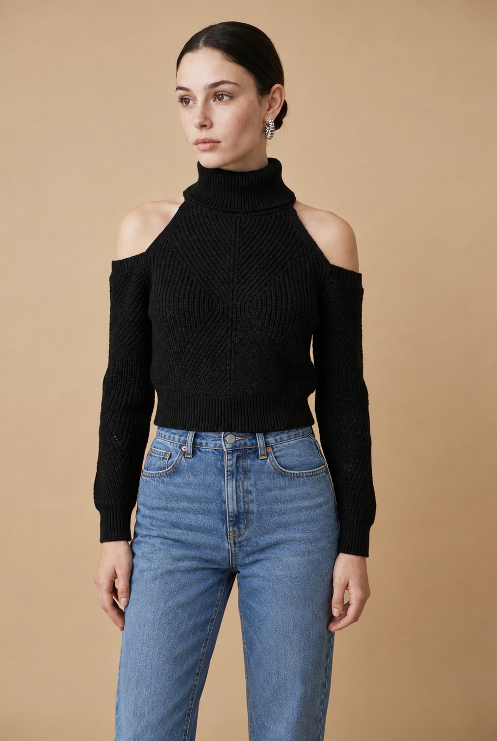 A woman wearing the Livigno cold-shoulder turtleneck sweater in black, showcasing its chic cut-outs and wide ribbed hem.