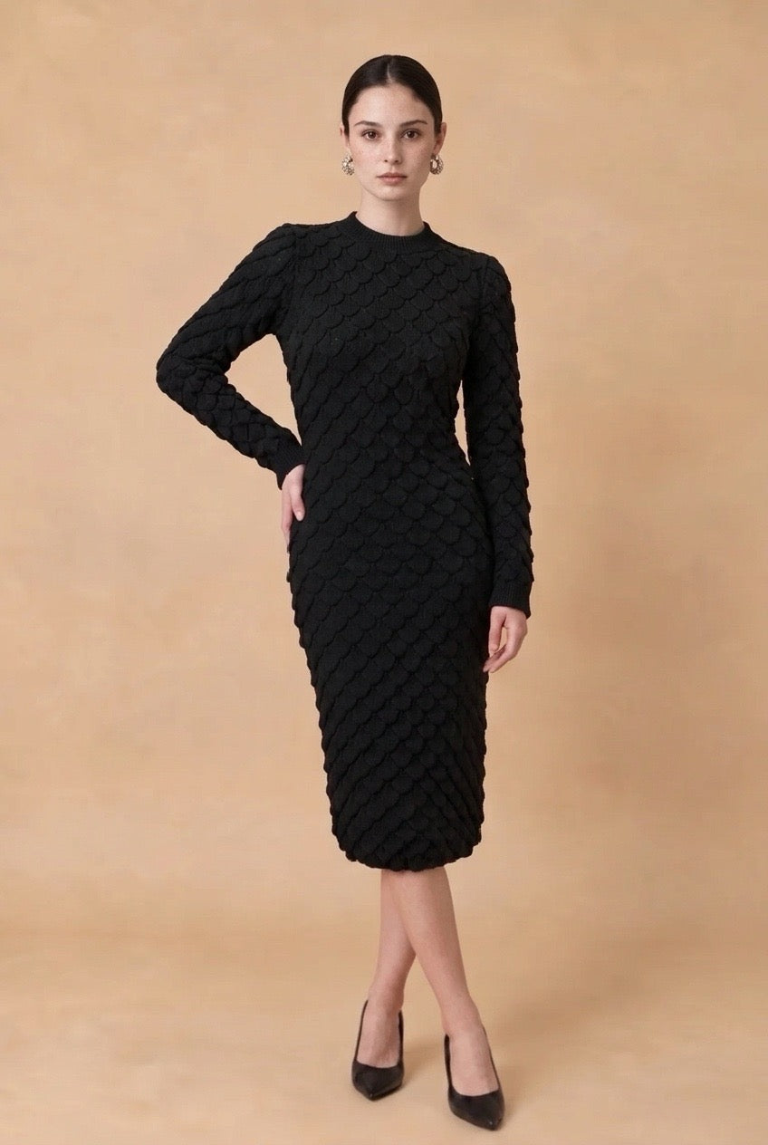 A woman wearing the Lucce long-sleeve knit midi dress in black, showcasing its textured pattern and sophisticated fitted silhouette.
