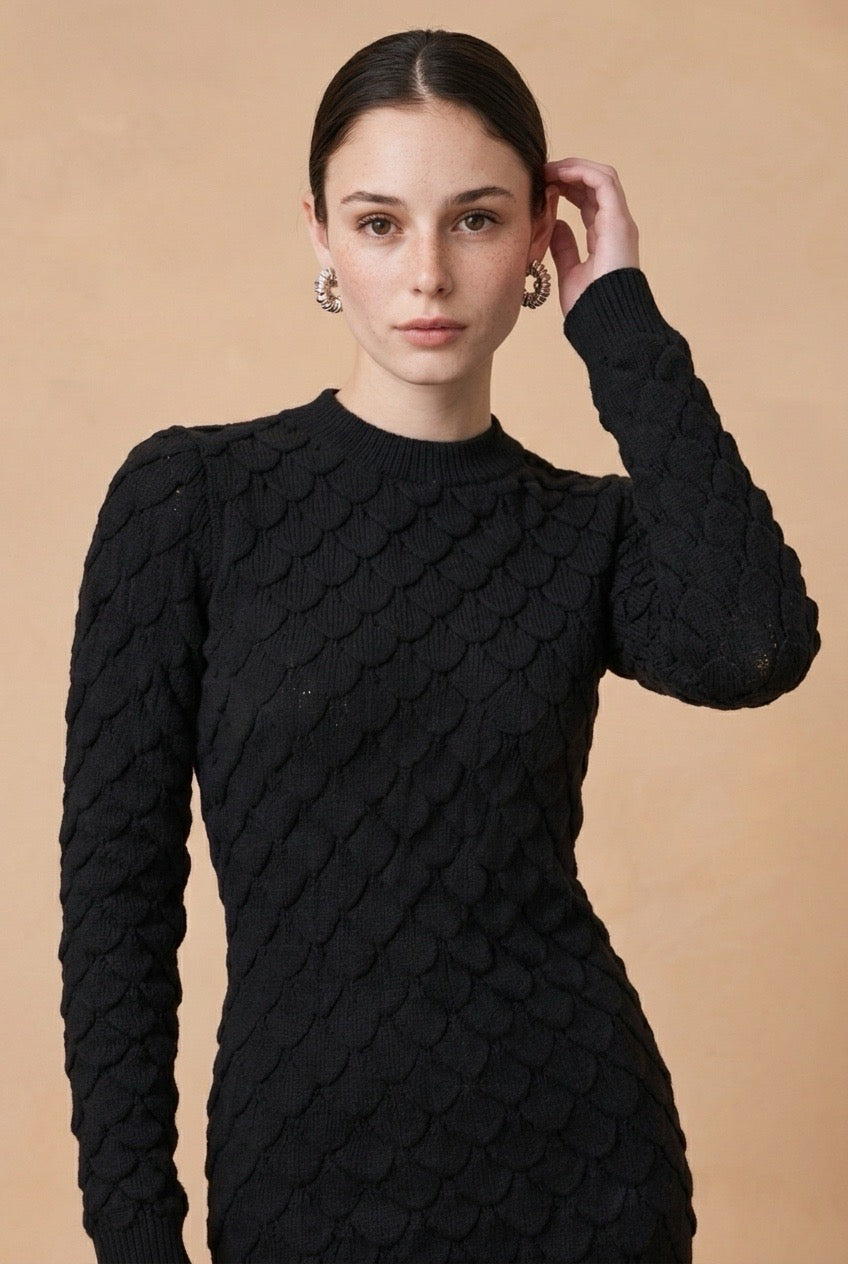 A woman wearing the Lucce long-sleeve knit midi dress in black, showcasing its textured pattern and sophisticated fitted silhouette.