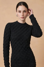 A woman wearing the Lucce long-sleeve knit midi dress in black, showcasing its textured pattern and sophisticated fitted silhouette.