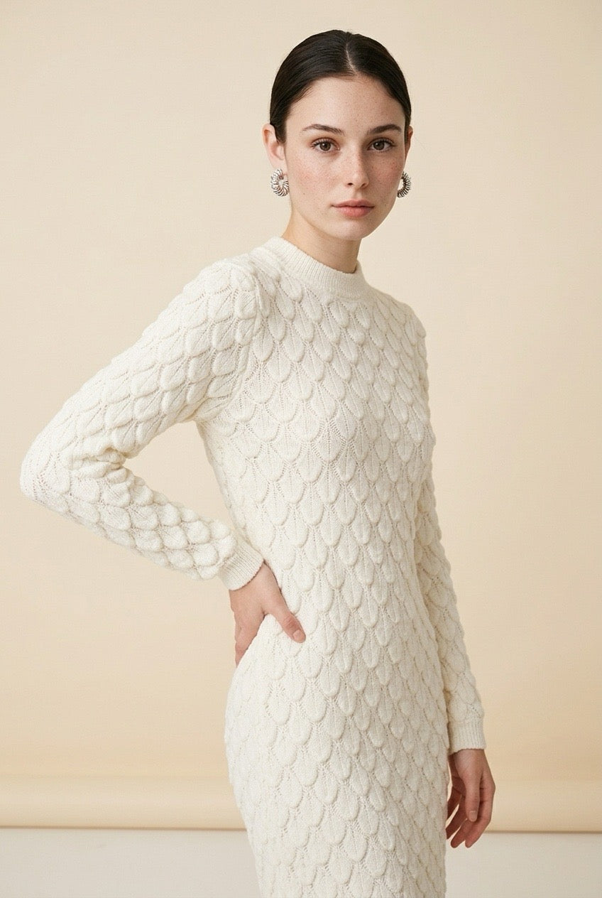 A woman wearing the Lucce long-sleeve knit midi dress in off-white, featuring a prominent 3D scallop cable texture and a classic crew neck.